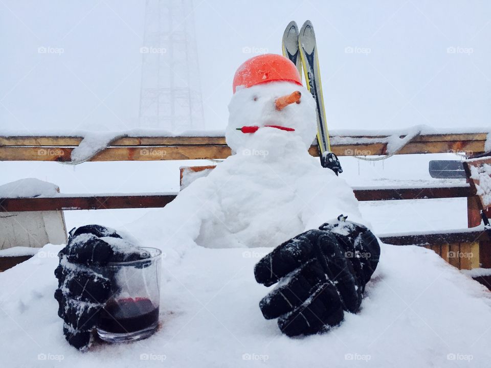 Funny snowman sitting at a table wearing gloves and holding a glass of drink