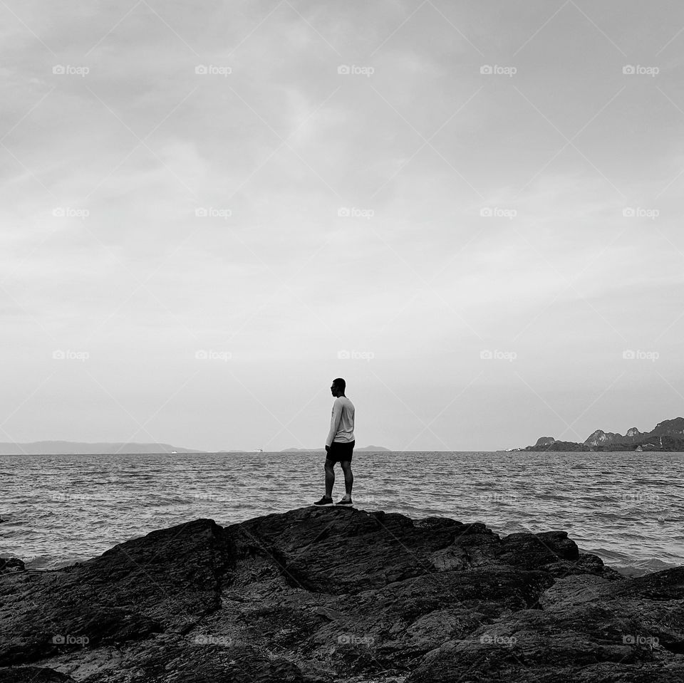 Man standing on stone at coastline