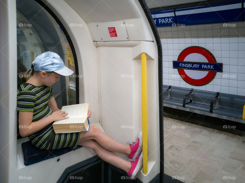 Girl reading book while commuting on tube, London underground. London. UK