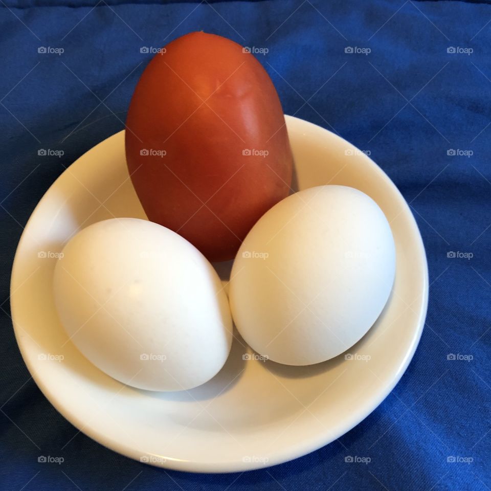 An Oval Shape Tomato And Two Eggs In A Circle Shape Bowl 