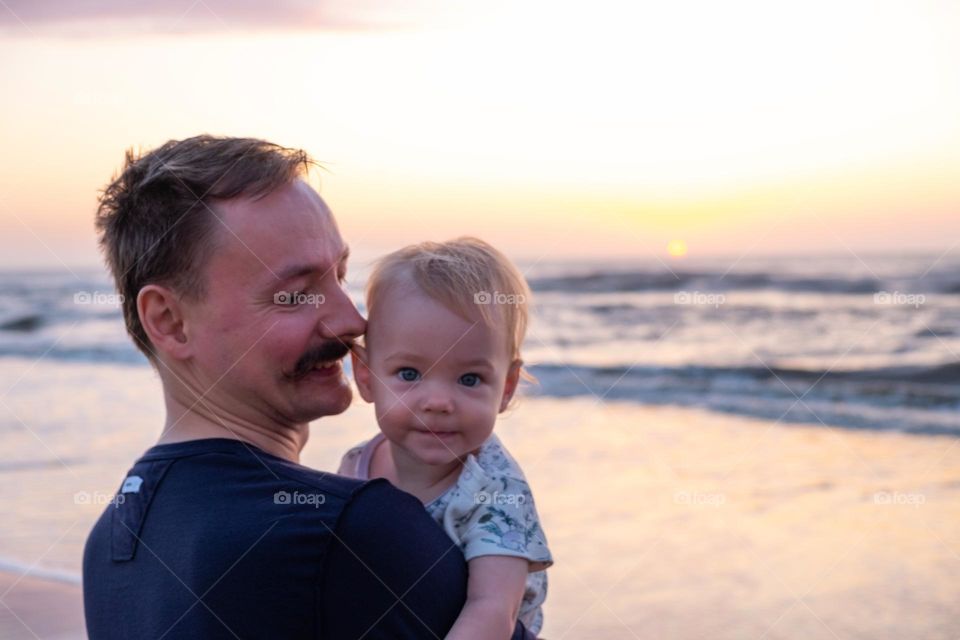 father holding a smiling baby on sunrise ocean background,family concept