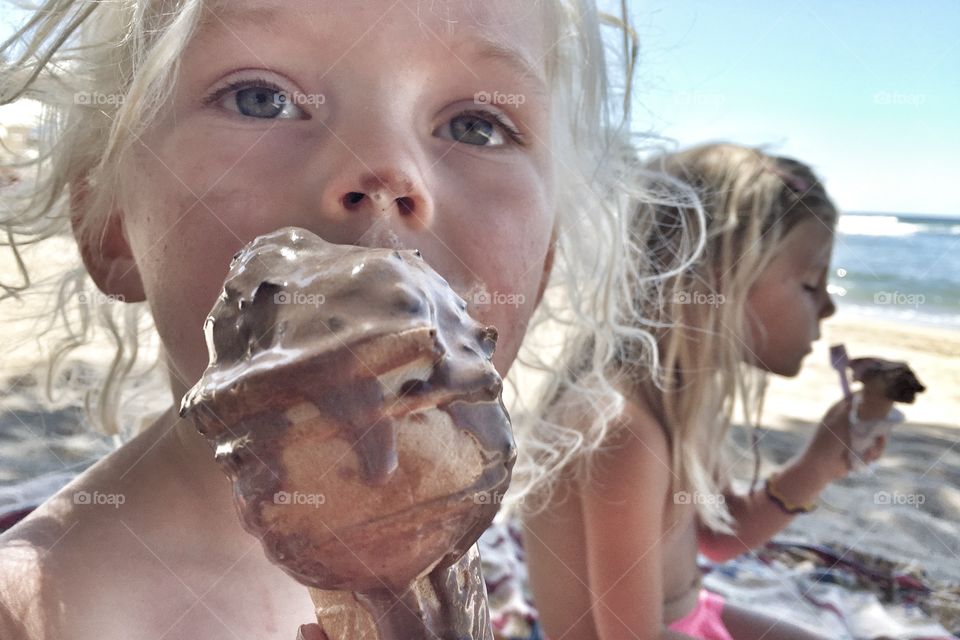 Messy girl eating ice-cream cone on beach