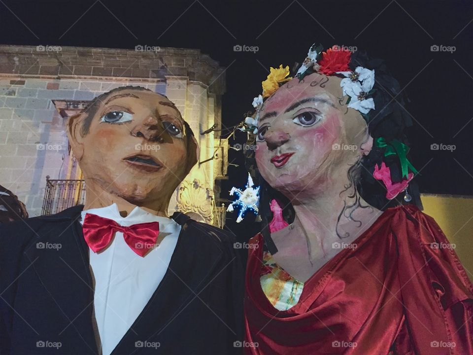Two giant papier-mâché- puppets (mojiangas) in formal  wear are attending an evening outdoor Christmas Celebration in City Centro ,San Miguel de Allende, Mexico.