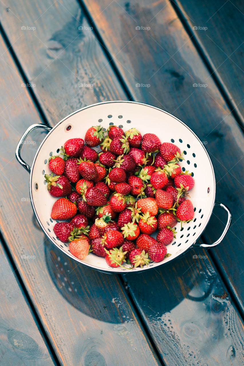 Closeup of bowl of fresh strawberries sprinkled raindrops on wooden table