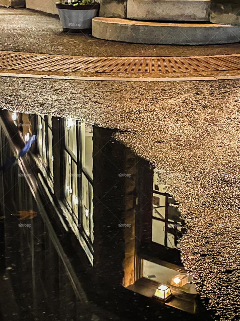 Reflection of a well lit building in a puddle from the evening rain.