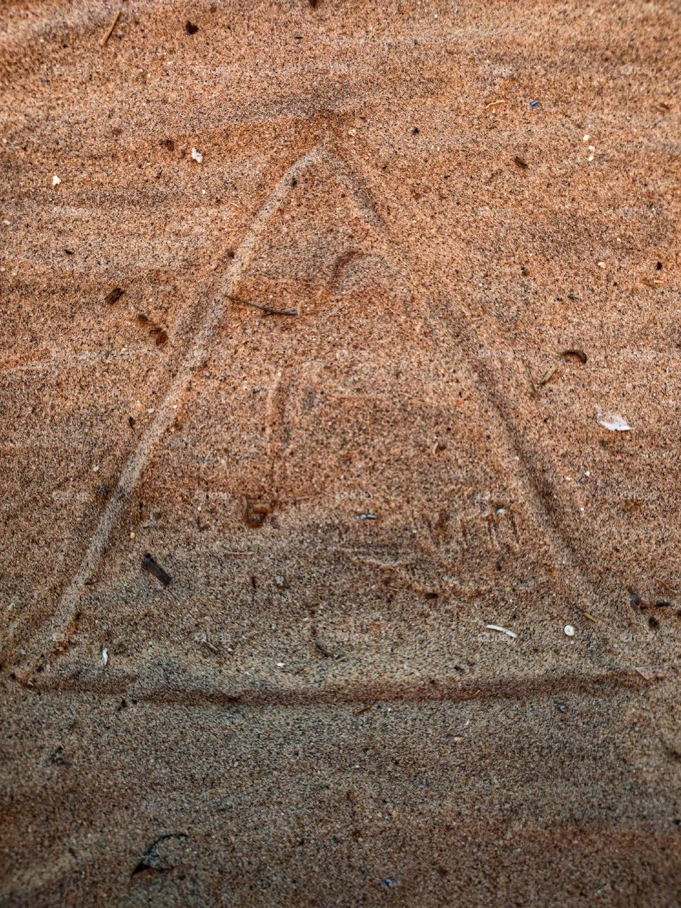 a simple drawing of a triangle made on the ground in the sands of the beach.