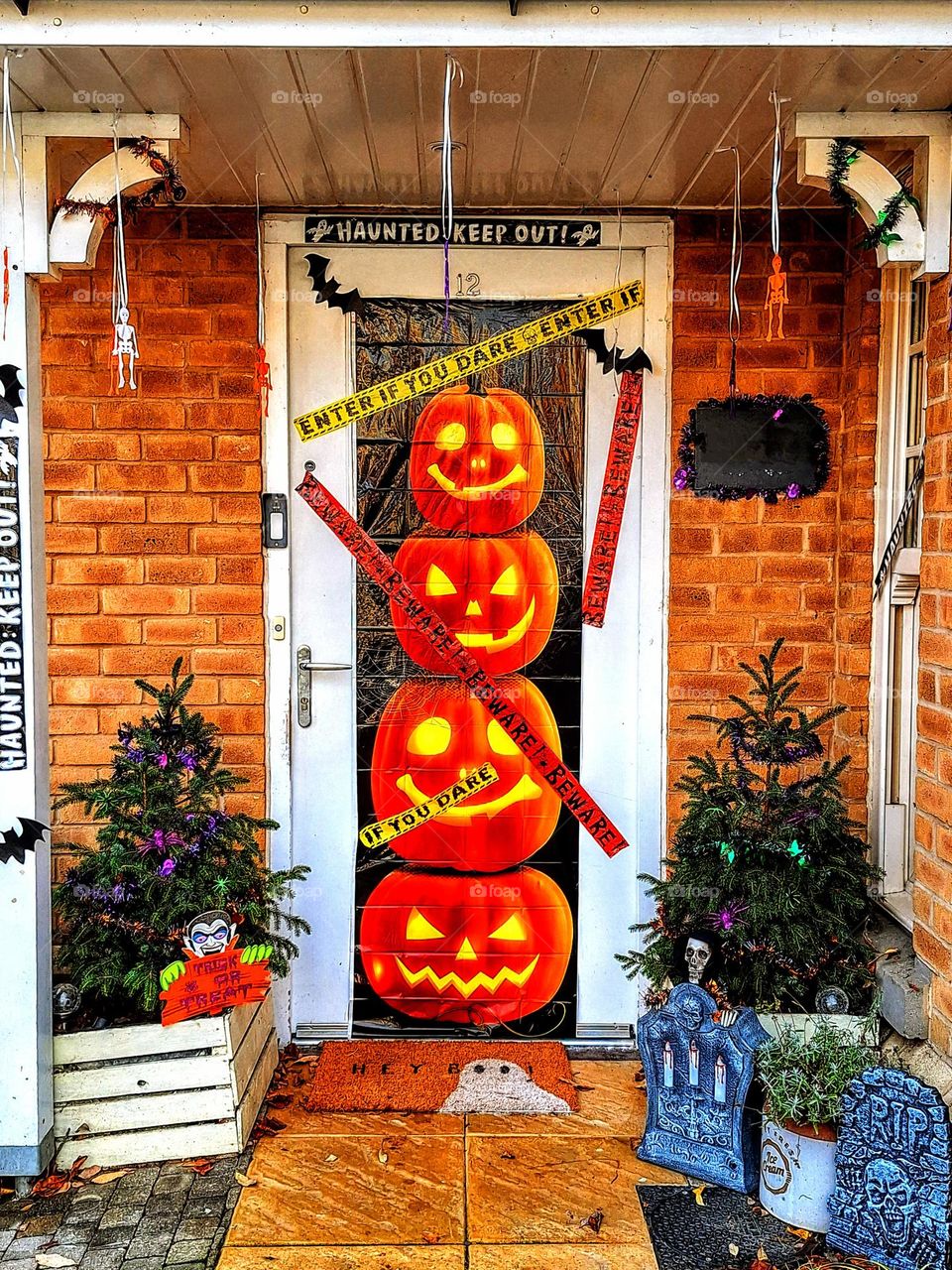 Halloween display with stack of brightly lit pumpkins, gravestones, mini Dracula, mini ghost and decorated mini Christmas trees