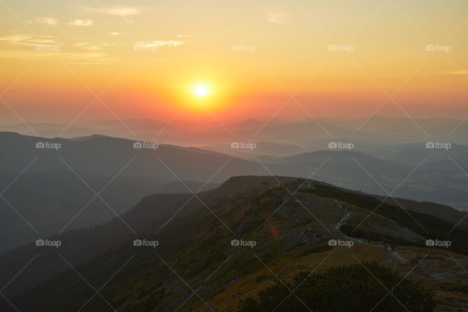 Sunrise in mountains. Natural mountain landscape with illuminated misty peaks, foggy slopes and valleys, blue sky with orange yellow sunlight. Amazing scene from Beskid Zywiecki in Poland