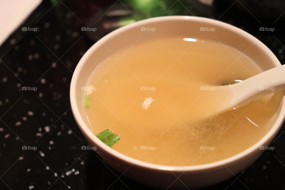 A close up of a hot bowl of miso soup with tofu and seaweed in a traditional Japanese bowl with spoon 