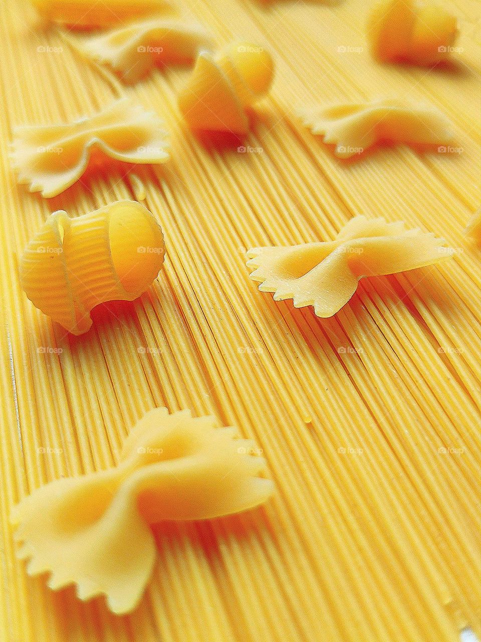 Pasta colors and shapes. On top of the spaghetti are Farfalle and Pipe Rigate pasta. Yellow explosion of different pasta