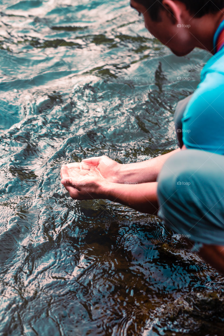 Young boy taking pure water from a river and holding it in the hands