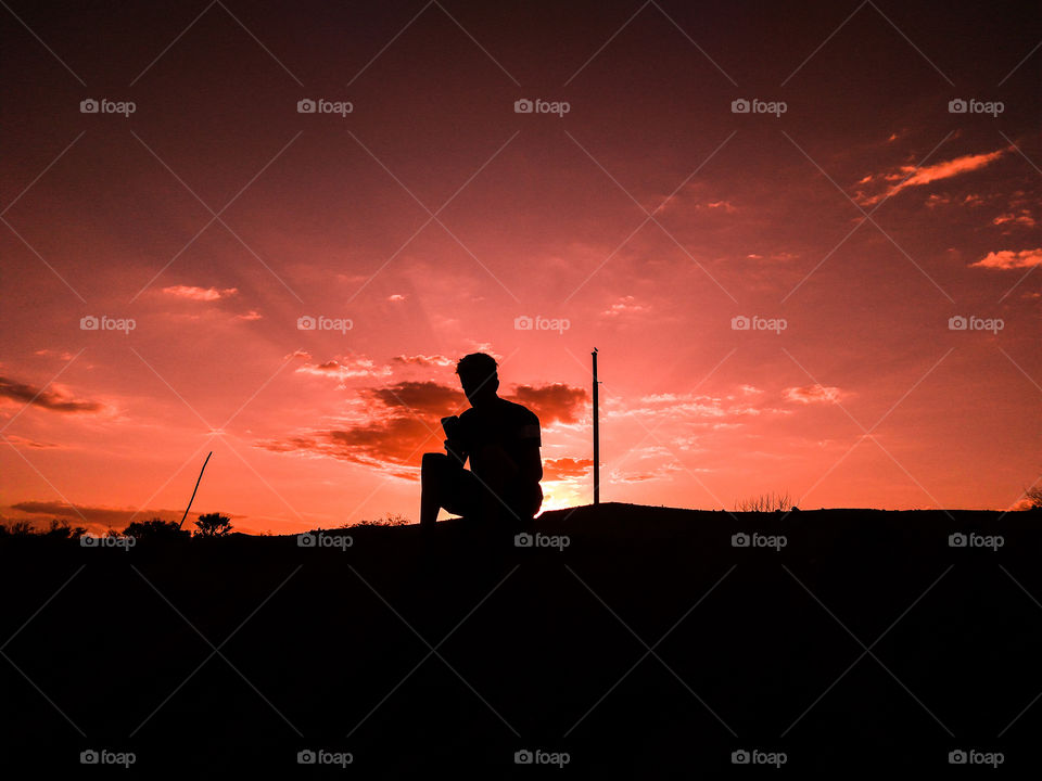 Silhouetted man using smartphone during sunset