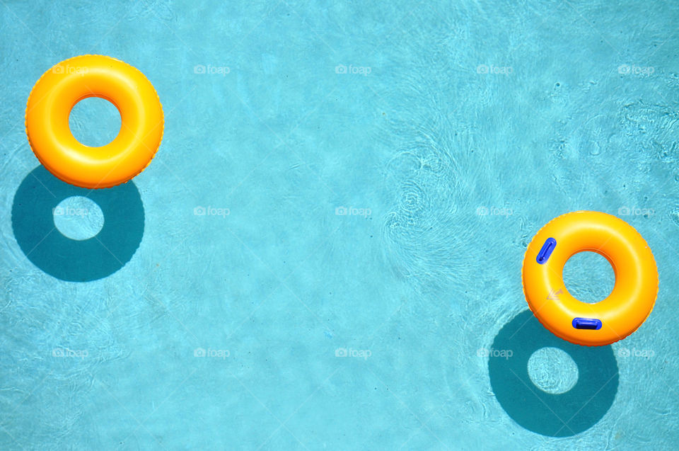 Two yellow pool rings / floats in a freshening cool blue swimming pool. Room for your copy space.