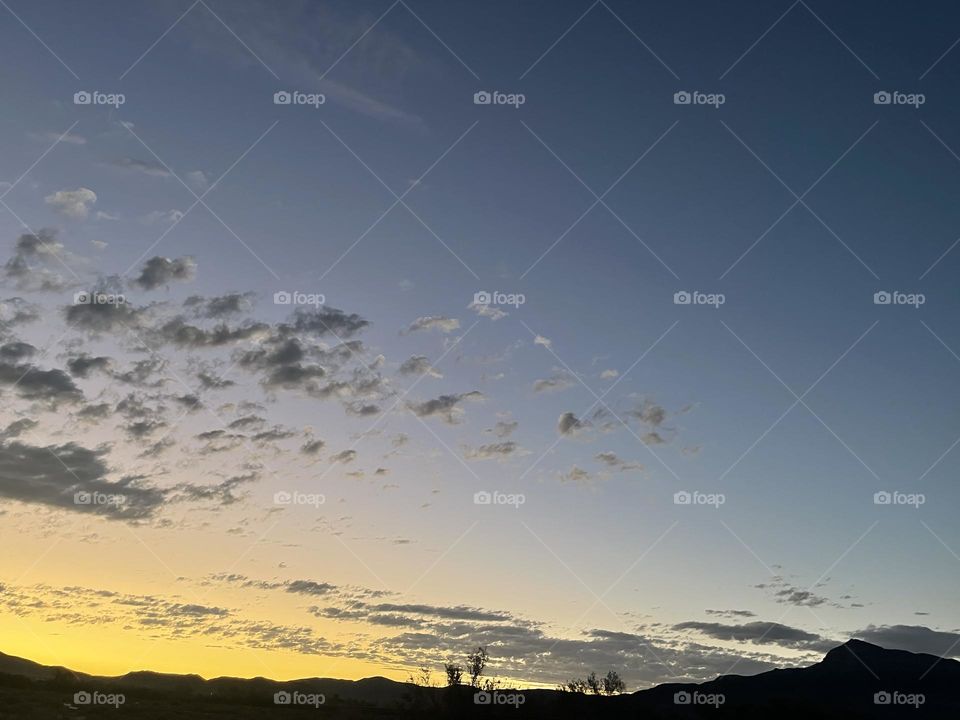 A yellow sunset with clouds, mountains, and trees.
