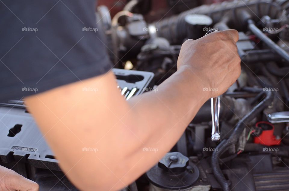 A man is working hard with car repairs to  his engine with a variety of tools as he attempts to install an alternator.
