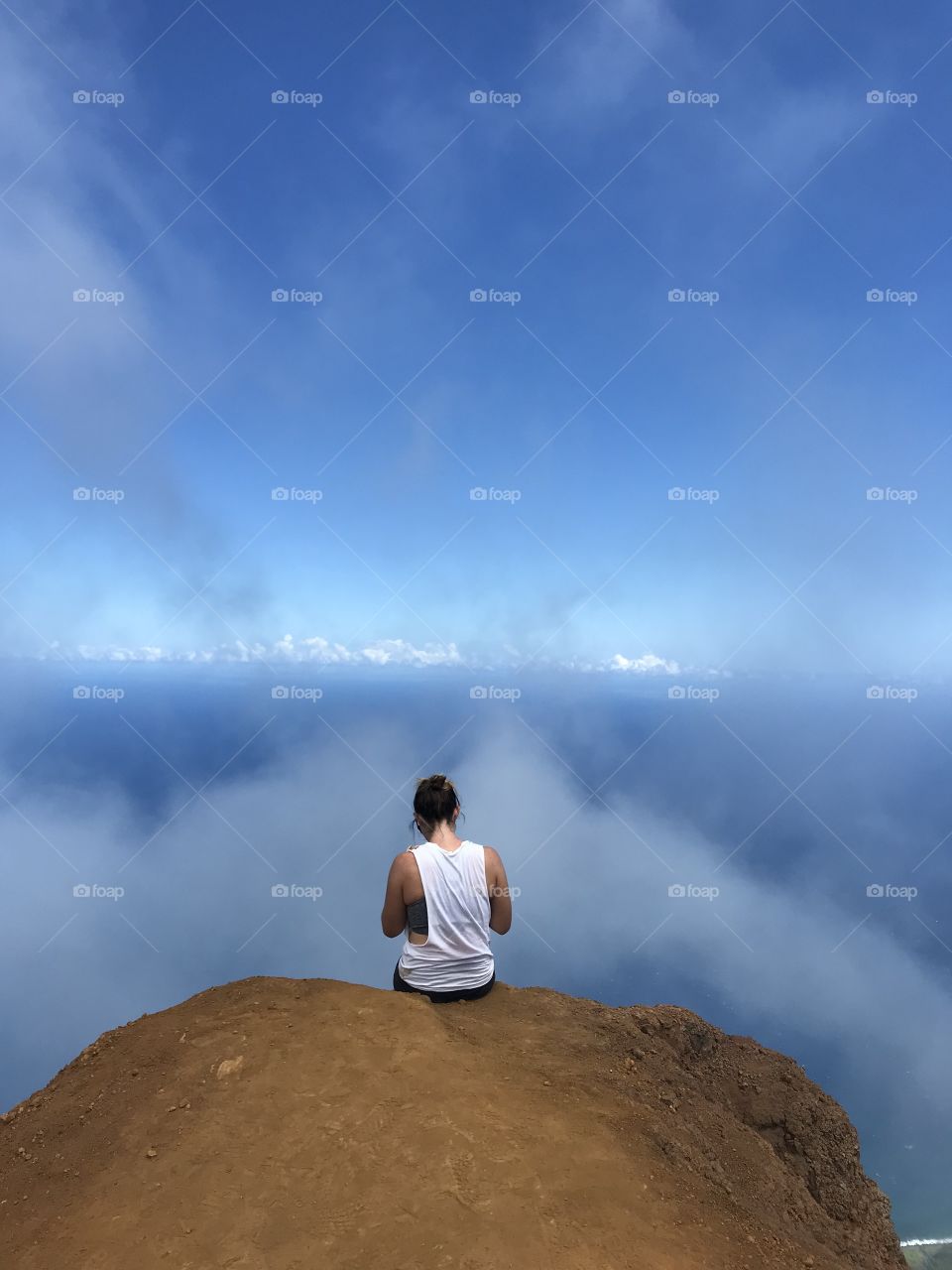 Mountain climber sits on the edge of the top of the mountain in the clouds in Hawaii.