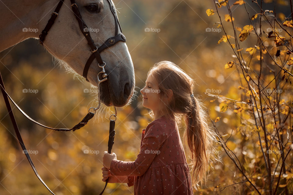 Little girl with grey horse in autumn park 