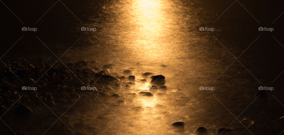 Shoreline at night. Long exposure of pebbles and the shoreline at night with the moon's reflection