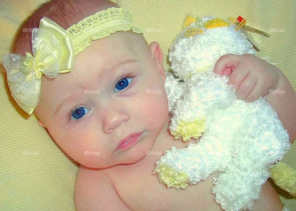 Baby girl lying on bed with toy and hair band