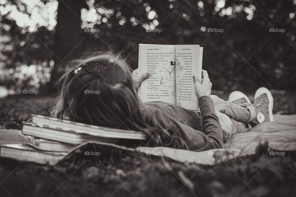 A girl laying on a blanket reading a book