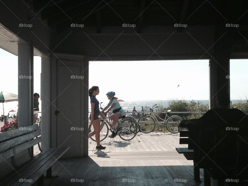 People walk and bike by on the boardwalk in Ocean Grove, NJ. Taken from outside the open-air Boardwalk Pavilion where people can sit, get some shade, and view the beach and ocean. Church services are held here in the summertime.