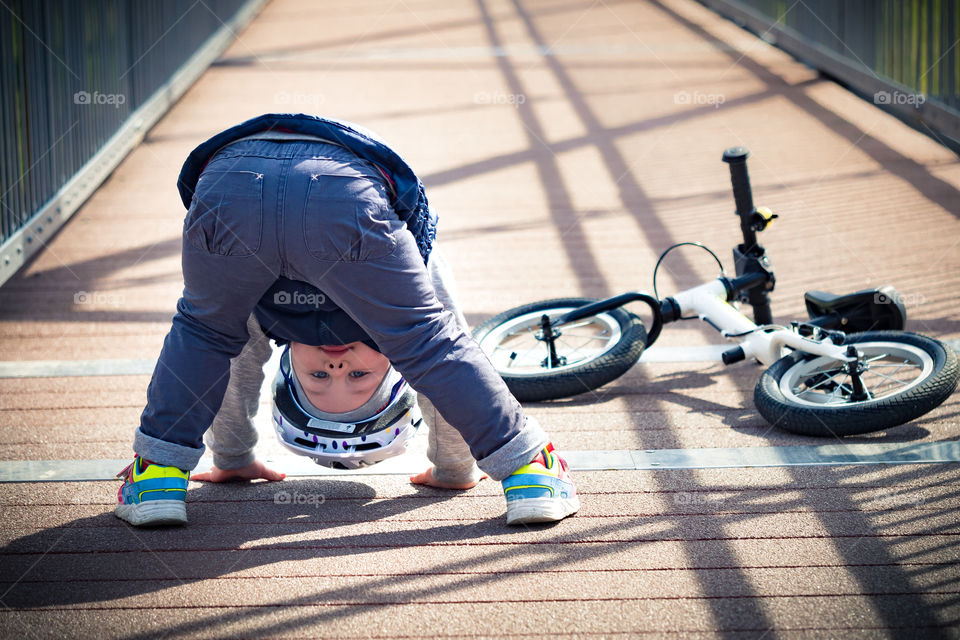Close-up of cute boy bending on boardwalk with bicycle