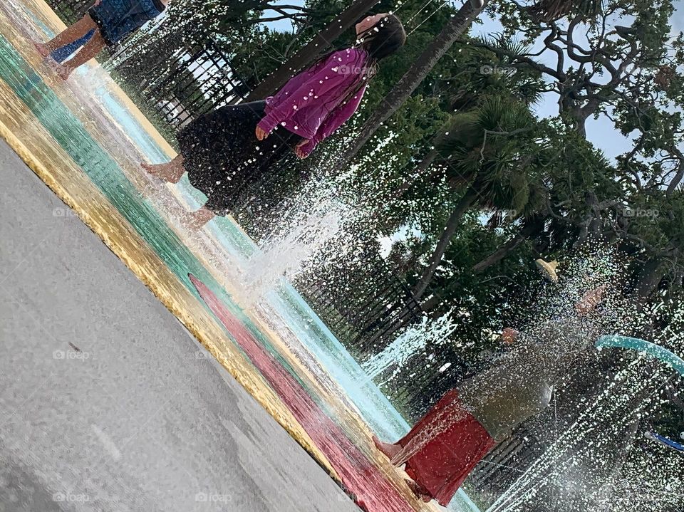 Children having lots of fun in the water at the colorful kids splash pad at the city park for children during a really warm day in Florida.