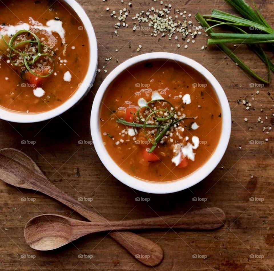 Tomato lentil soup in white bowls, garnished with cashew cream and hemp seeds on a wood table.