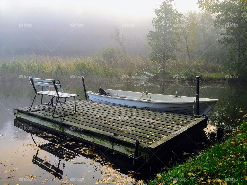 Battle: summer vs autumn: silent autumn landscape with wooden pier, boat and bench reflecting in the still calm water 