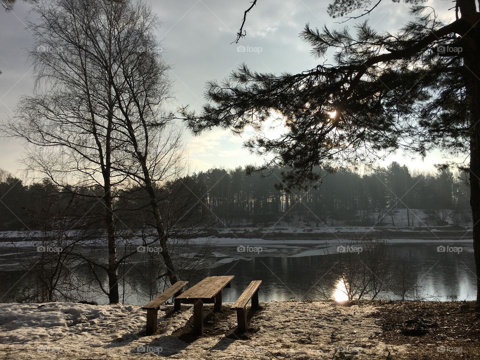 Wooden bench in front of river during winter