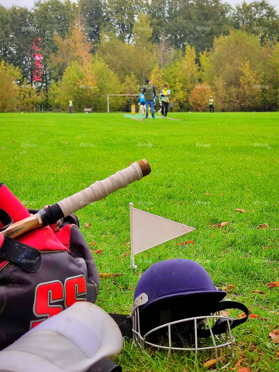 Cricket game.  Field with players.In the foreground a protective helmet and a bag with sports equipment