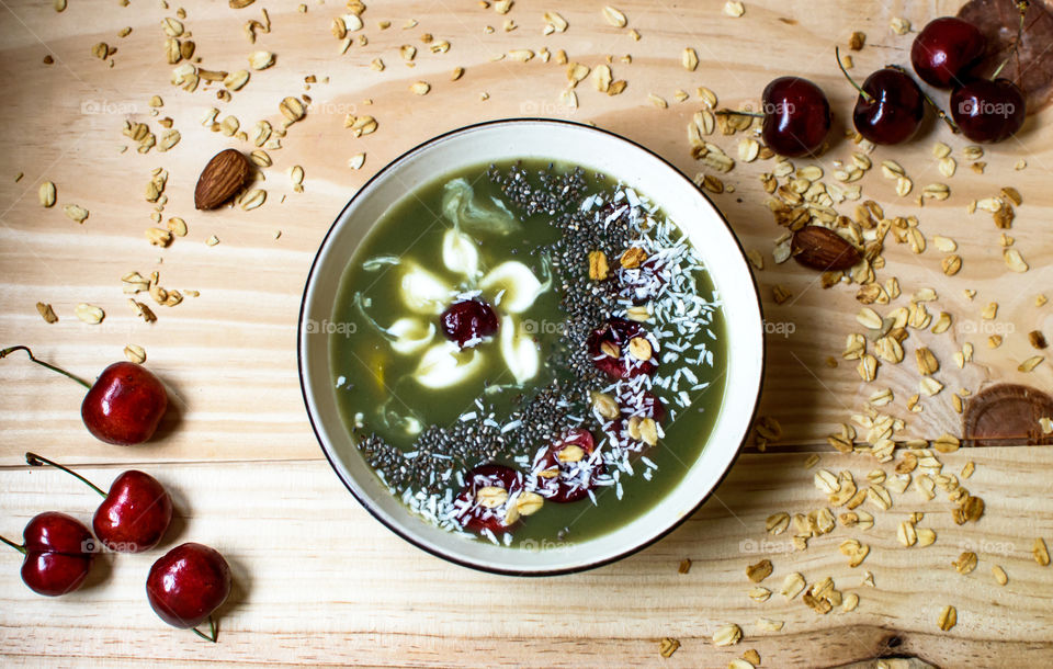 Beautiful artisanal green smoothie bowl photography conceptual healthy lifestyle background with elegant garnish items chia, oatmeal,dark cherry sliced, yogurt, coconut sprinkles, almonds and honey and fresh fruit ingredients