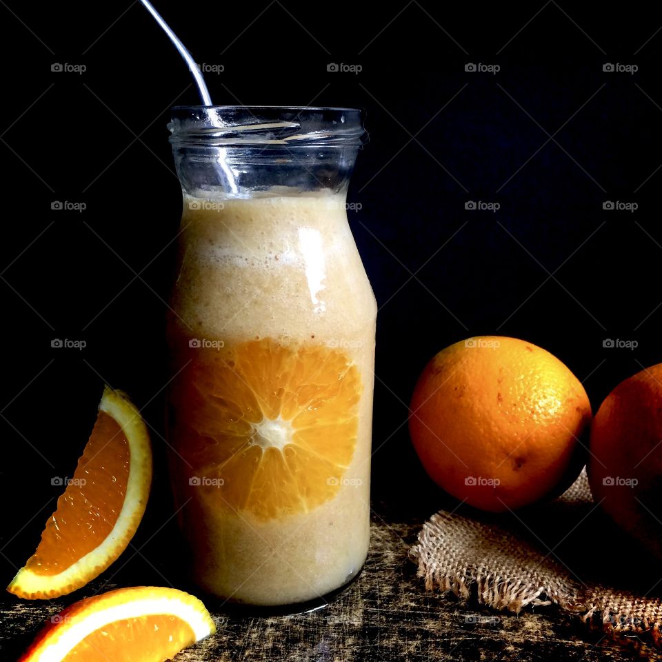 Orange and banana smoothie in a glass jar with straw and a sliced orange showing through glass.