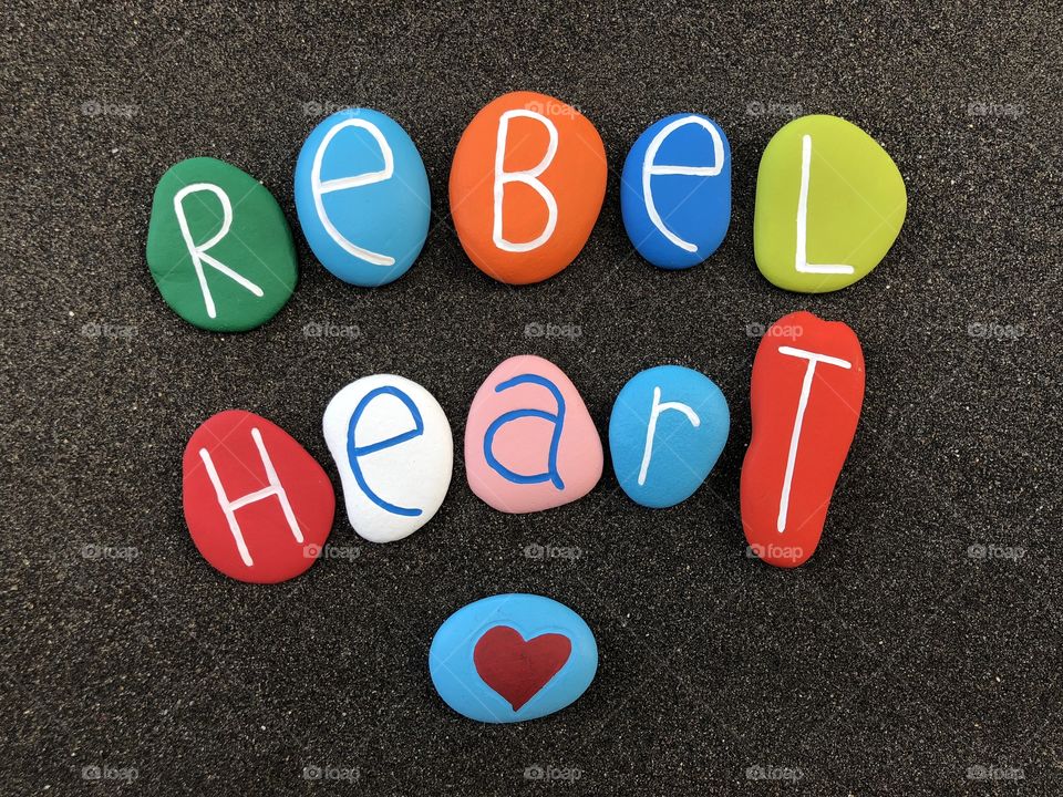 Rebel heart text with colored stones over black volcanic sand