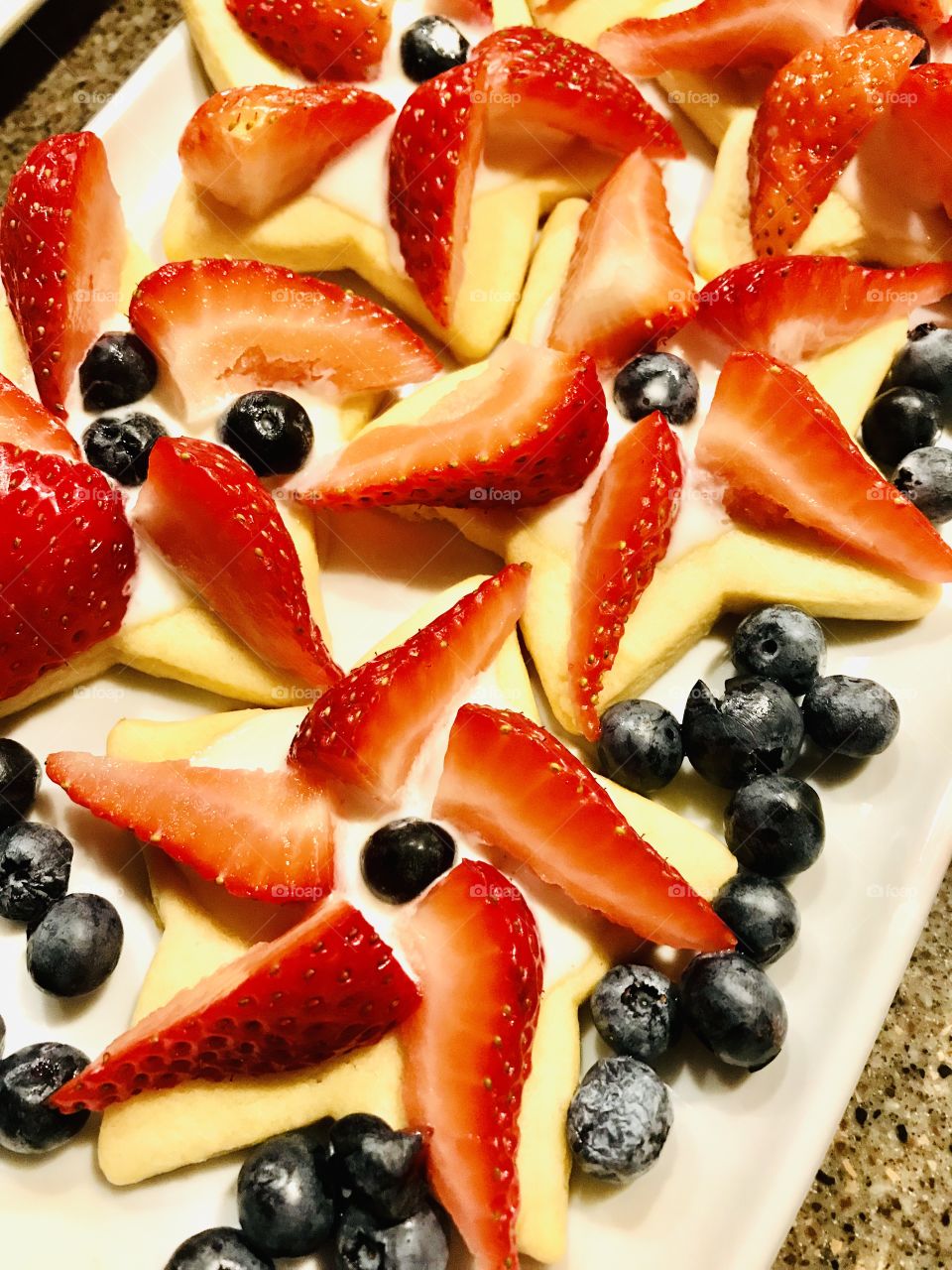 Plate of delicious star sugar cookies topped with bright red juicy strawberries and beautiful dark blue blueberries perfect for the Patriotic holiday!!