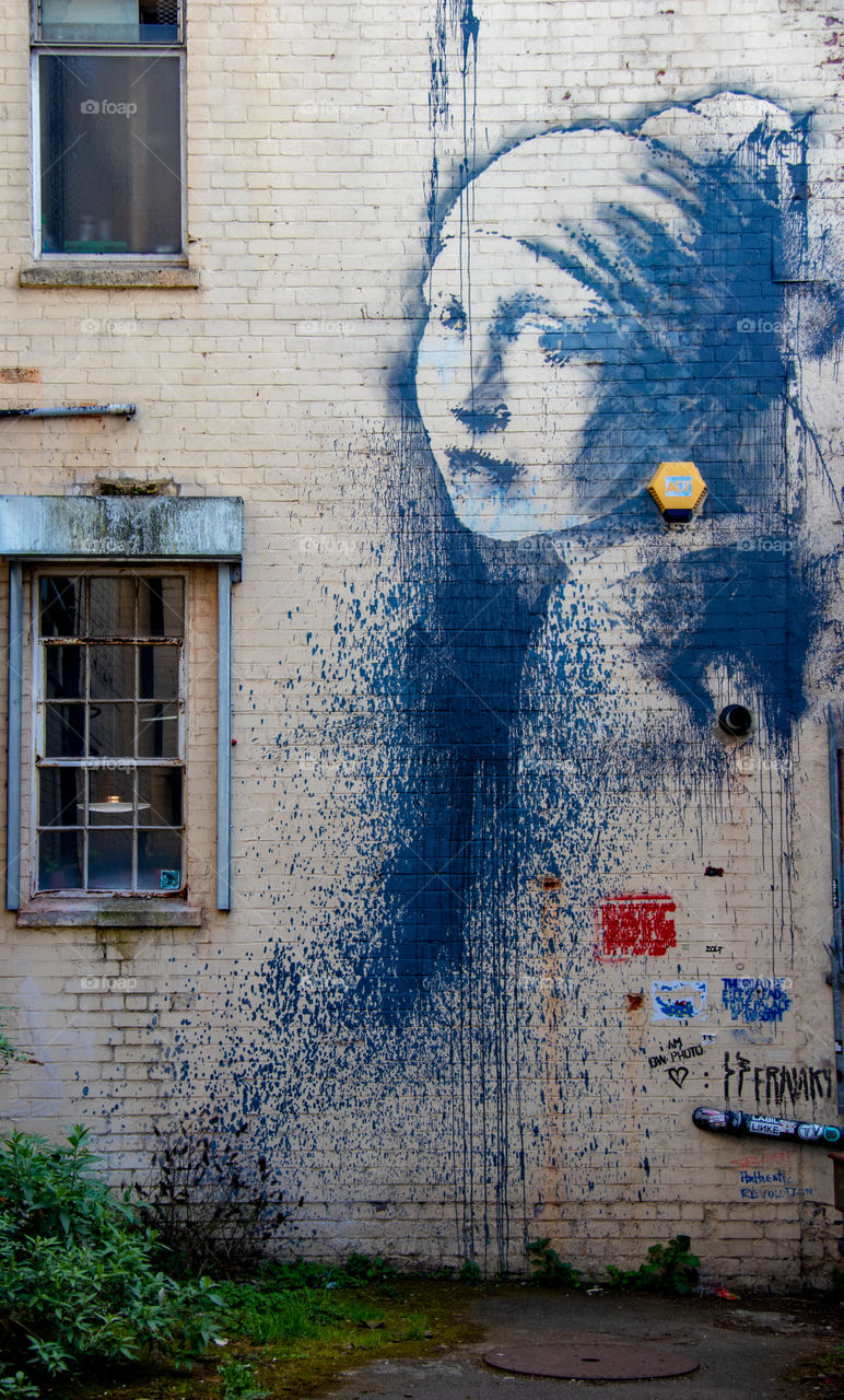 Girl with the pierced eardrum by Banksy. graffiti on the side of the wall in Bristol by famous street artist Banksy. Colourful adaption of the famous Girl with the pearl  earring.