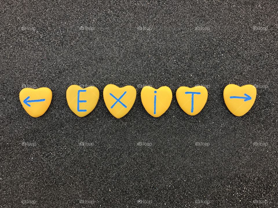 Exit ways text with yellow colored heart stones over black volcanic sand