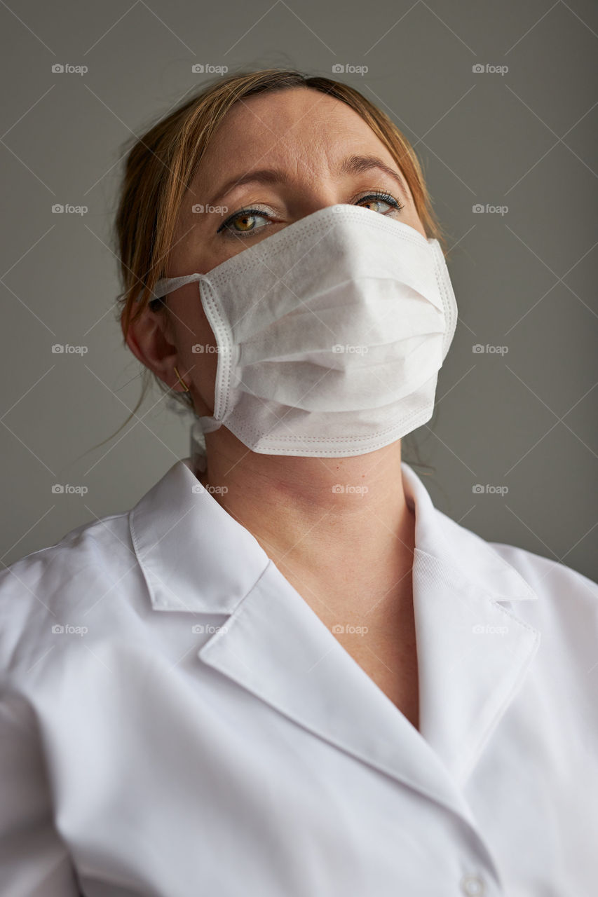 Doctor with face covered with mask. Portrait of young woman wearing the uniform, cap and mask to avoid virus infection and to prevent the spread of disease. Real people, authentic situations