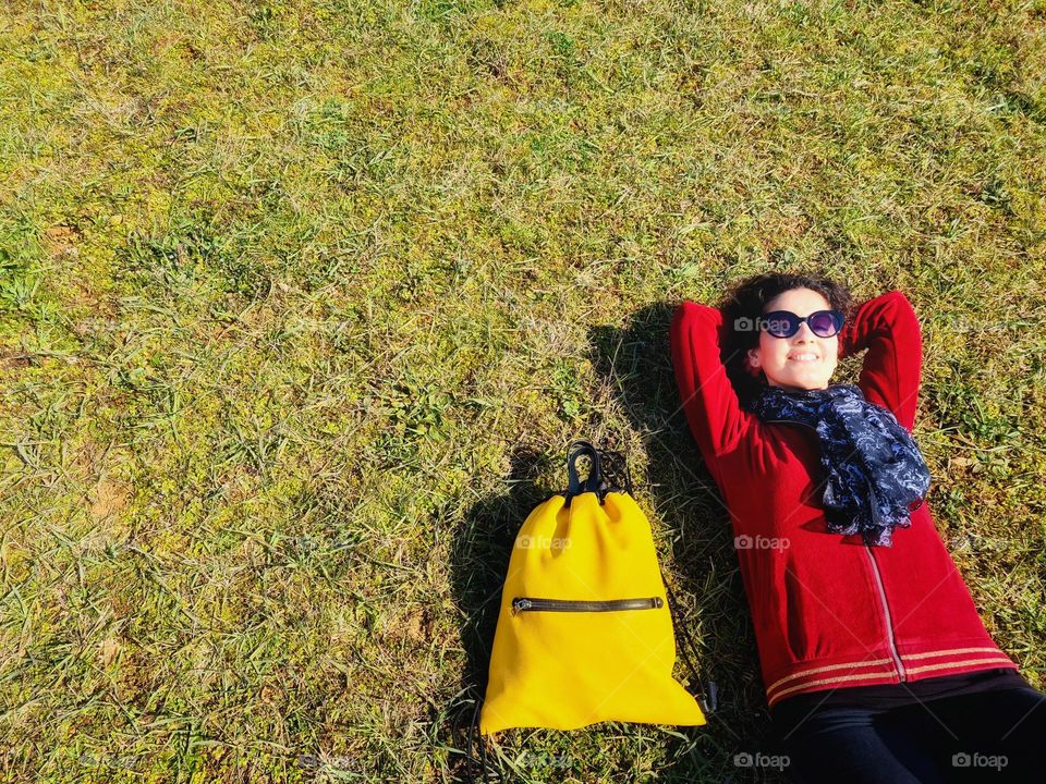 smiling woman with yellow backpack relaxes on the meadow