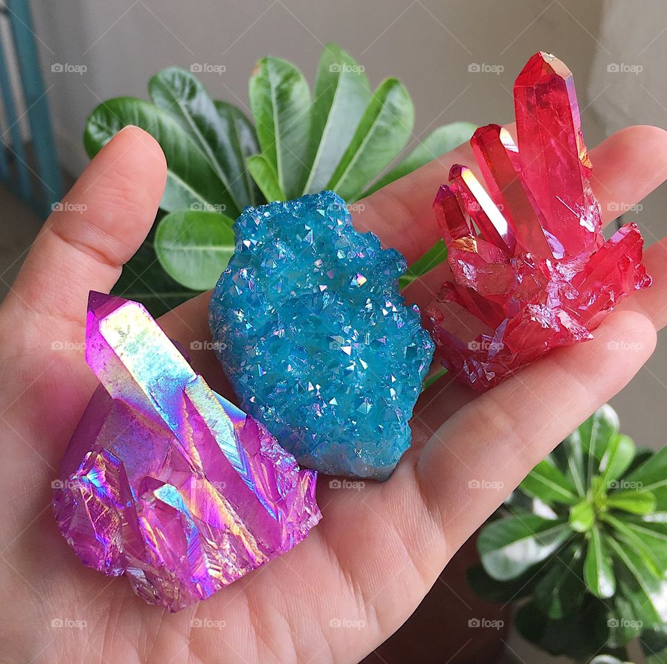 Purple, blue and red angel aura crystal clusters resting on a palm.
