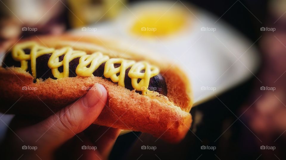 A hand holding a bratwurst sandwich with spicy mustard on a wheat roll yum