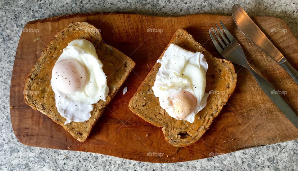 Poached eggs on toast on olive wood with cutlery 