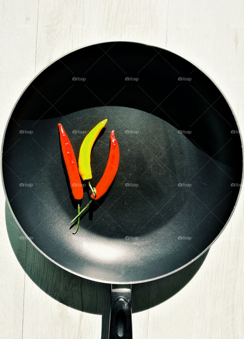 red and yellow chilli on dark frying pan with light wooden background