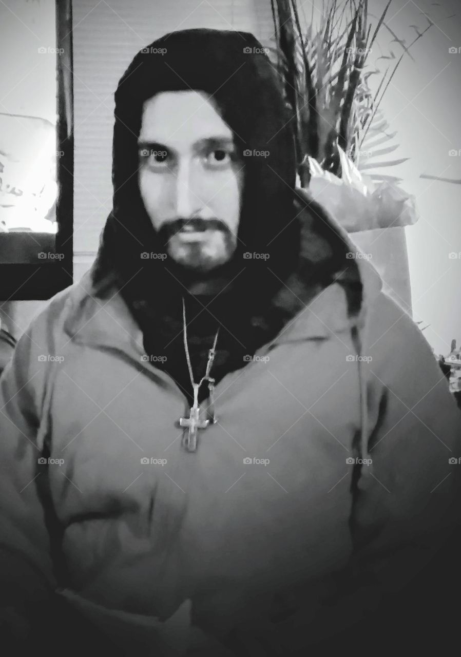 A younger man, dressed warmly for the cold weather, with a cross pendant worn outside of his coat, taken in black and white.