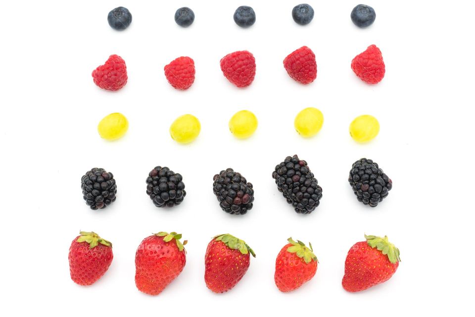Diferent types of fruits arranged in lines: strawberries, blackberries, grapes, raspberries and blueberries. White background