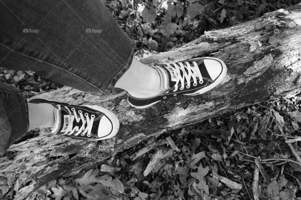 A person standing on tree trunk with wearing all star shoes