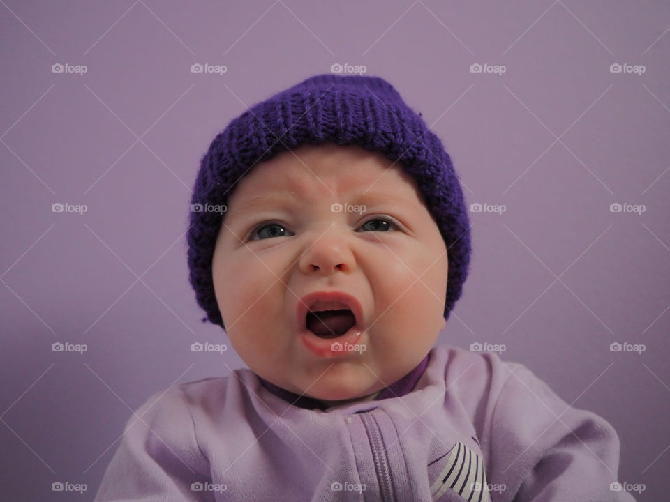 Little baby making funny face while wearing purple hat