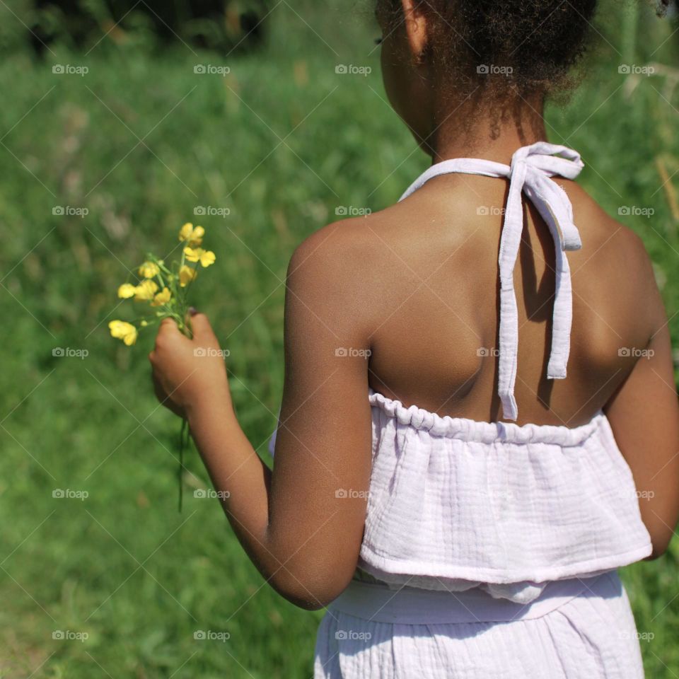 Girl of mixed race picking wildflowers in a barley field during summer time