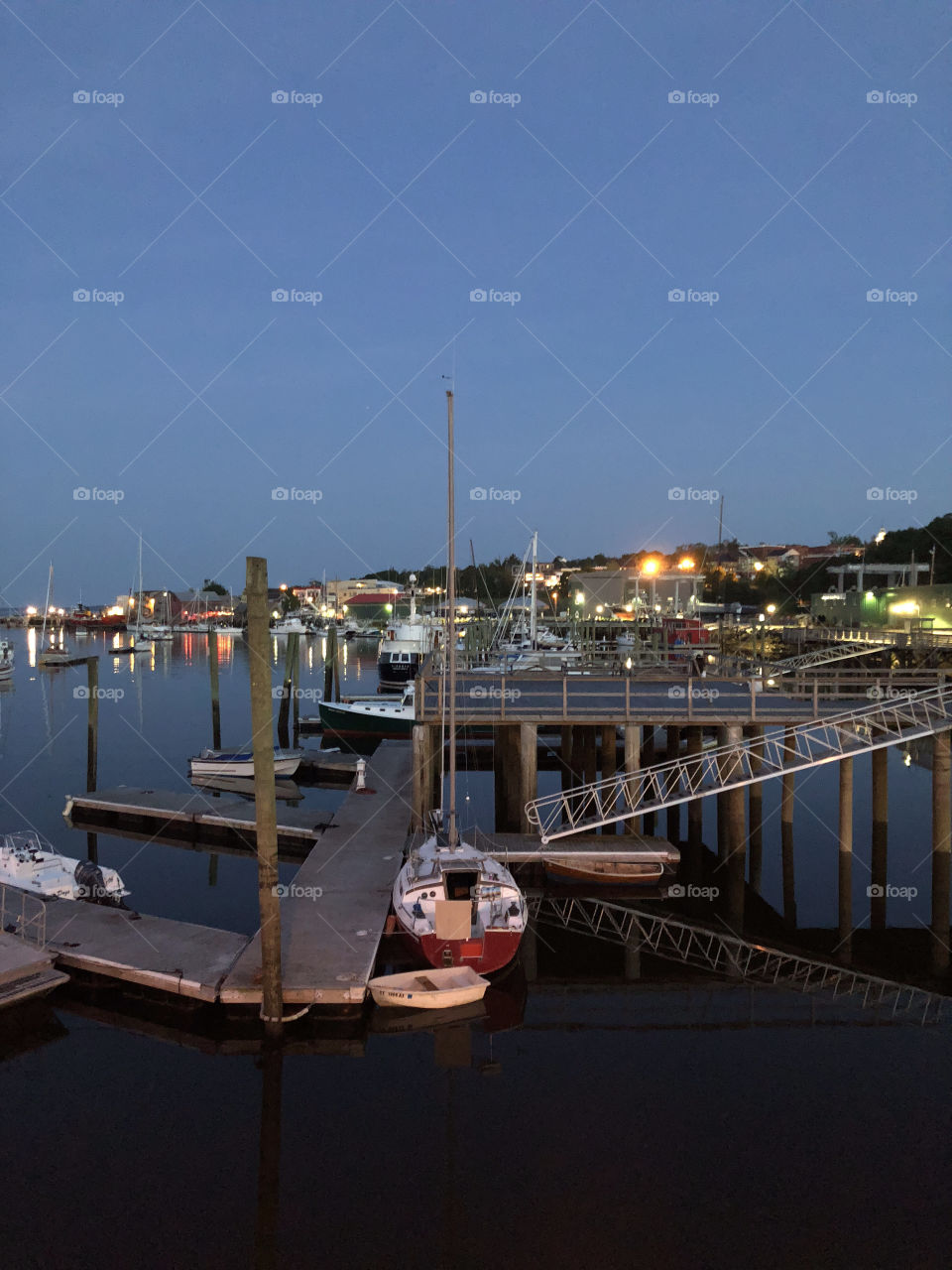 Belfast Harbor and shipyard in Belfast, Maine on a summer evening after sunset, with the city lights reflecting on the water, and boats docked onsite
