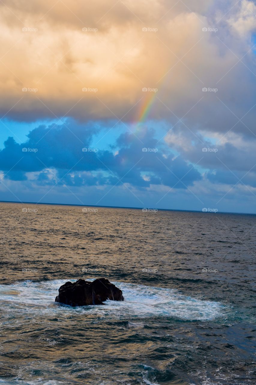 Rainbow at dusk lined up with an outcropping of lava rock on the island of Hawaii 